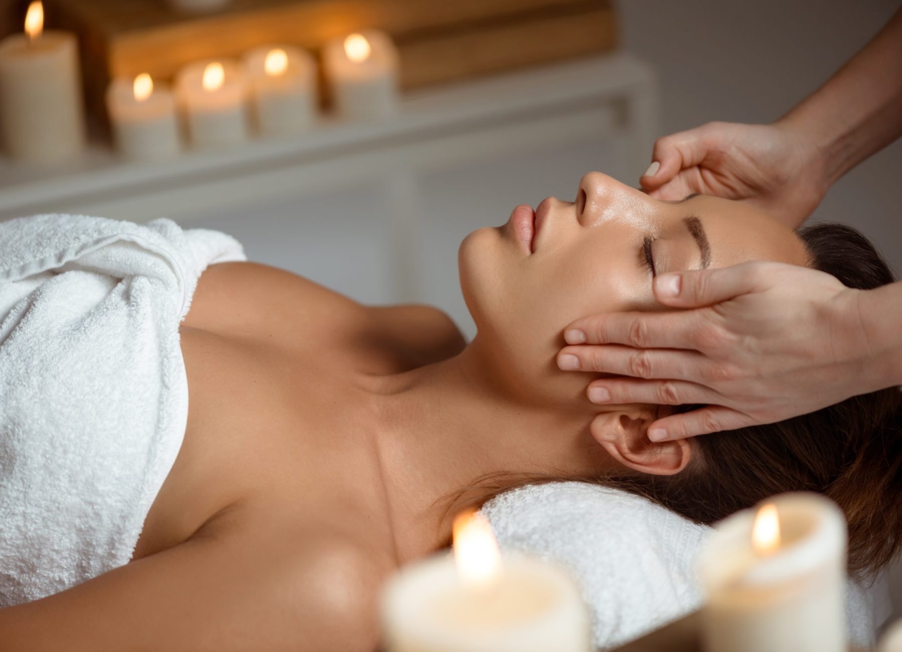 Young beautiful brunette girl having face massage relaxing in spa salon. Eyes closed. Copy space.